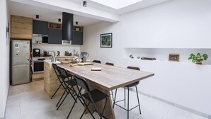 Eine moderne Küche mit Oberlicht, Holzschränken, einem Esstisch mit Stühlen und einer kleinen Kücheninsel mit Geräten.