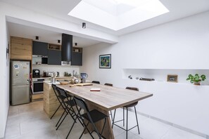 A modern kitchen with a skylight, wooden cabinets, a dining table with chairs, and a small island with appliances. - Charming house between Hossegor golf and Capbreton with patio under the pines (CAPBRETON)