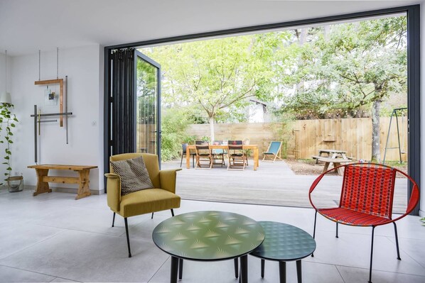 A modern interior with a glass door leading to a patio area, a wooden bench, a yellow armchair, and a red chair. - Charming house between Hossegor golf and Capbreton with patio under the pines (CAPBRETON)