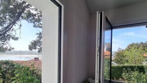 Ein Zimmer mit Fensterblick auf einen Garten und ein Gewässer, ein Toaster auf einem Regal und eine Tür mit Griff.
