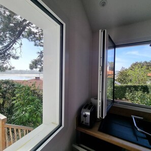 Ein Zimmer mit Fensterblick auf einen Garten und ein Gewässer, ein Toaster auf einem Regal und eine Tür mit Griff.