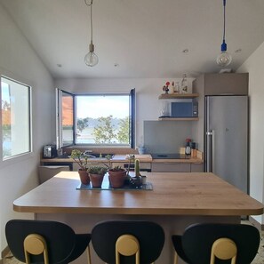 Una cocina moderna con una isla grande, un comedor con sillas, un ventanal con puerta abierta y un refrigerador.