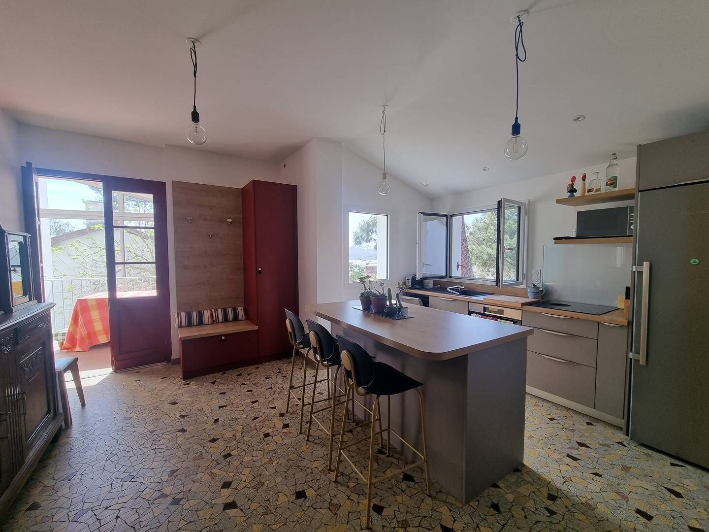 Eine moderne Küche mit Kochinsel, Barhocker, einem Essbereich mit einer Bank und einem großen Fenster für natürliches Licht.