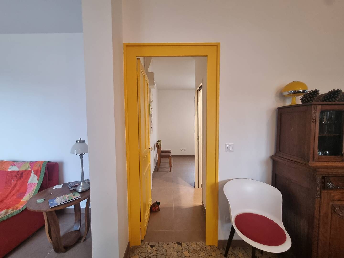 Ein Zimmer mit einem roten Sofa, einem kleinen Holztisch, einem weißen Stuhl, einer gelben Tür und einem Schrank mit Kiefernzapfen.