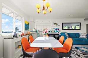 A modern kitchen with white cabinets, a dining area with a white table and orange chairs, and a blue sofa in the living room.