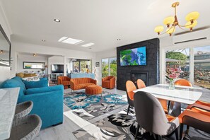A modern living room with a fireplace, a television, and a dining area with orange chairs.