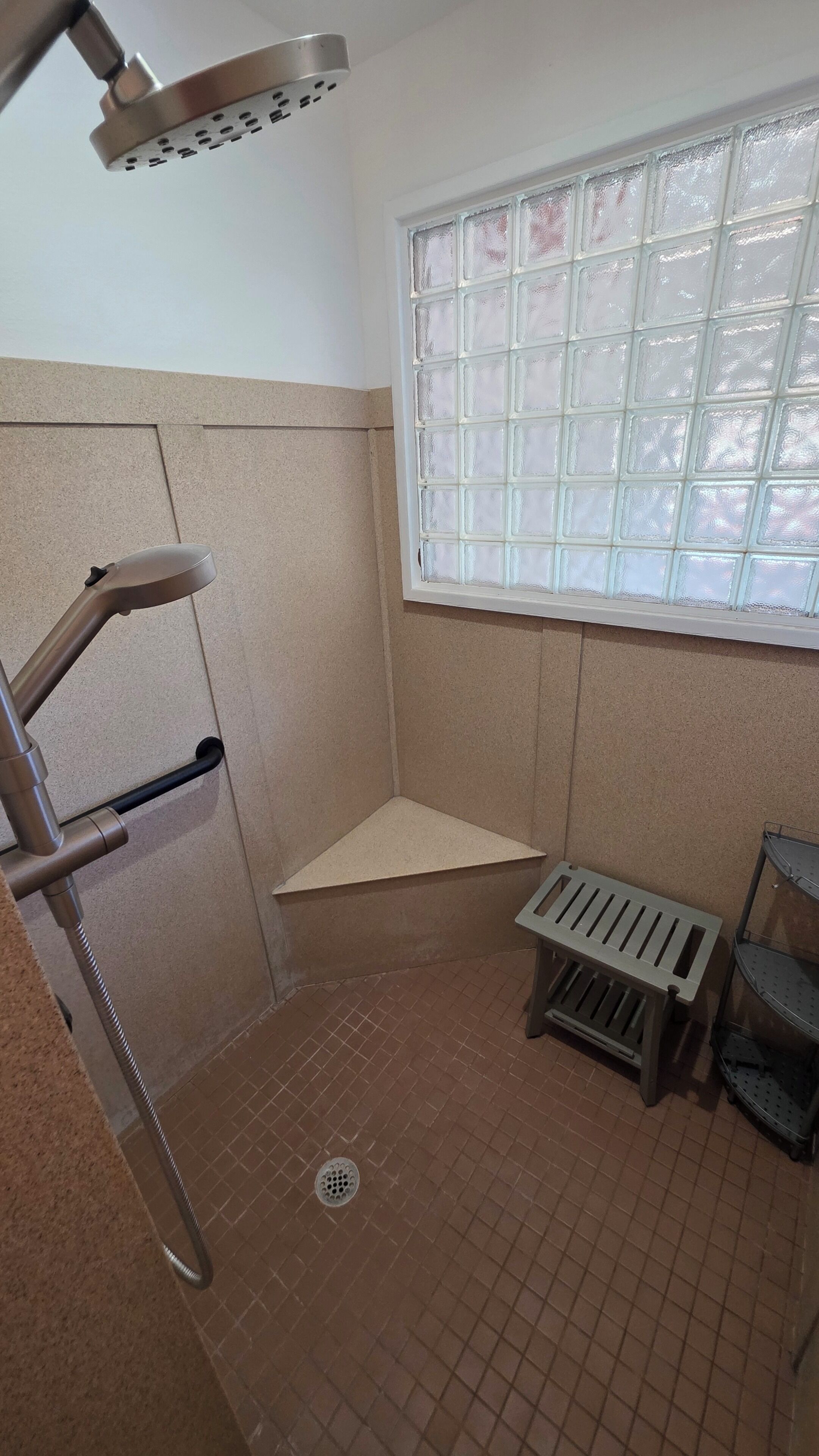 Un baño pequeño con ducha, ventana y un banco de metal.