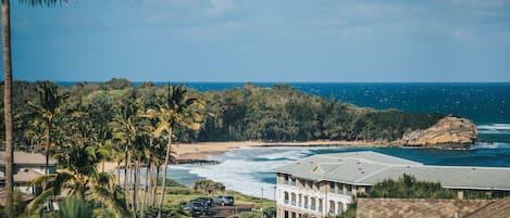 A coastal hotel with a view of the ocean, a beach, and a rocky outcrop.