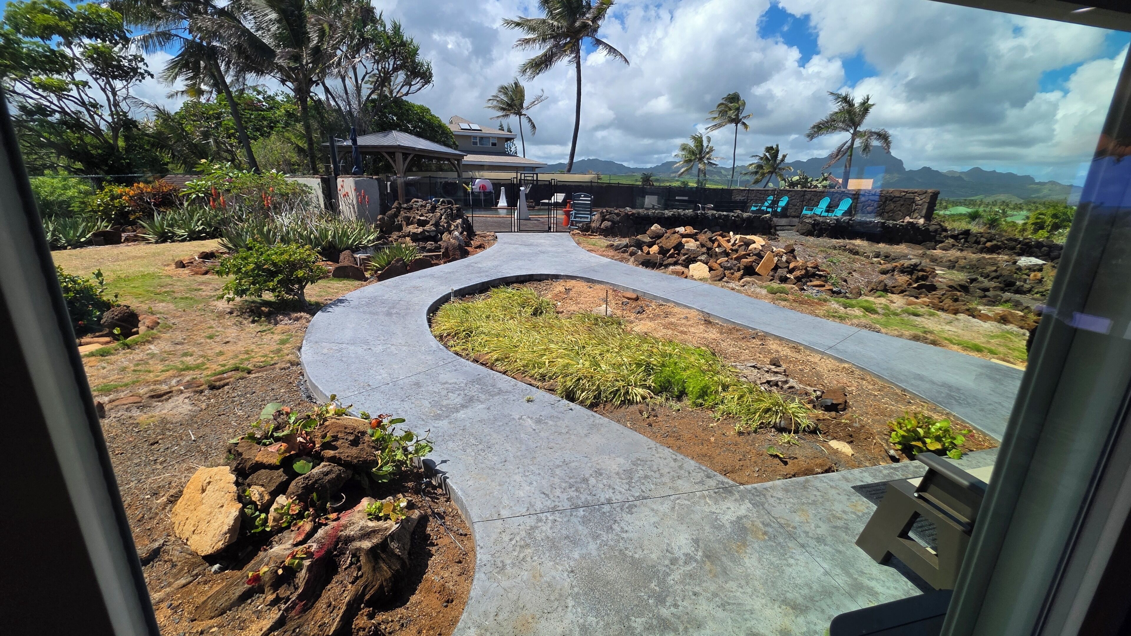 Un camino conduce a un edificio con una zona techada, rodeado de vegetación tropical y palmeras.