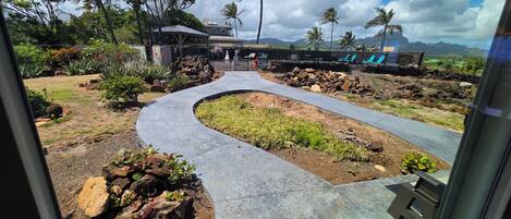 Un camino conduce a un edificio con una zona techada, rodeado de vegetación tropical y palmeras.