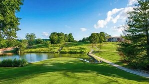 Een golfbaan met een vijver, bomen en een gebouw op de achtergrond.