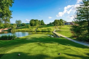 Ein Golfplatz mit Teich, Bäumen und einem Gebäude im Hintergrund.