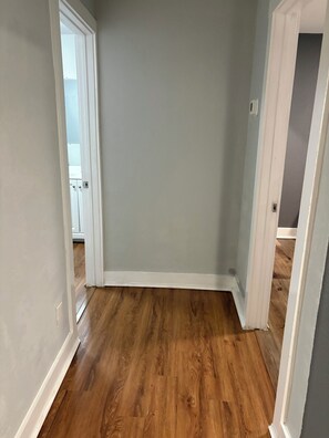 Un pasillo con piso de madera, molduras blancas y pared gris.
