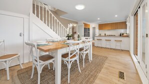 Ein Essbereich mit Holztisch und weißen Stühlen, eine Treppe sowie eine Küche mit Holzschränken.