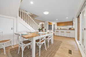 Ein Essbereich mit Holztisch und weißen Stühlen, eine Treppe sowie eine Küche mit Holzschränken.