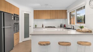 Eine moderne Küche mit einem Edelstahl-Kühlschrank, Holzschränken, einer großen Kochinsel mit Hockern und einem Fenster mit Aussicht.