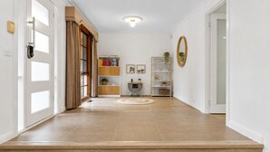 Ein Flur mit Holzboden, einer Tür mit Griff, einem Bücherregal, einem kleinen Tisch mit Pflanze und einem Spiegel an der Wand.