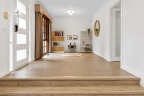 Ein Flur mit Holzboden, einer Tür mit Griff, einem Bücherregal, einem kleinen Tisch mit Pflanze und einem Spiegel an der Wand.