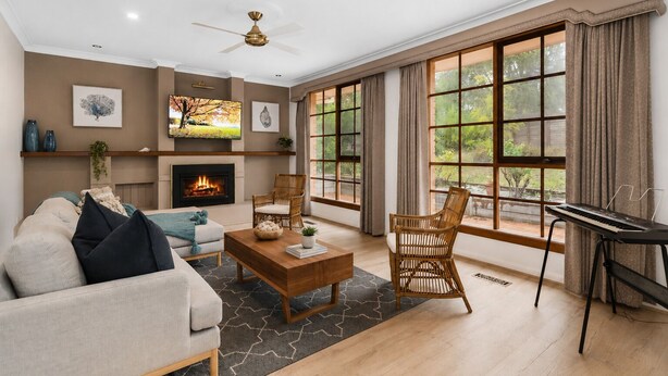 Ein Wohnzimmer mit Kamin, Fernseher, Klavier und großen Fenstern mit Vorhängen.