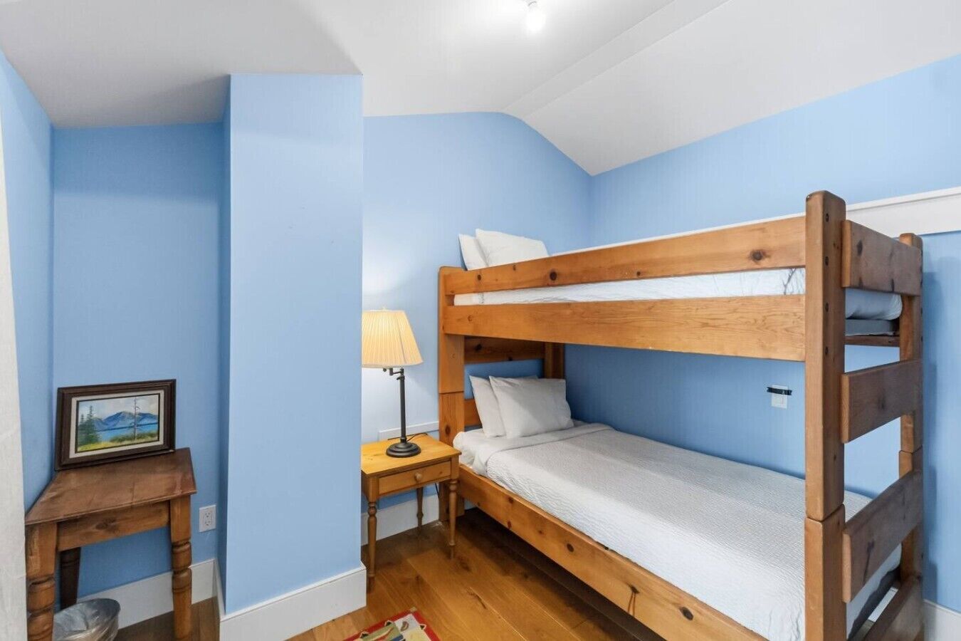 Een slaapkamer met een stapelbed, een nachtkastje, een lamp en een lijst aan de muur.