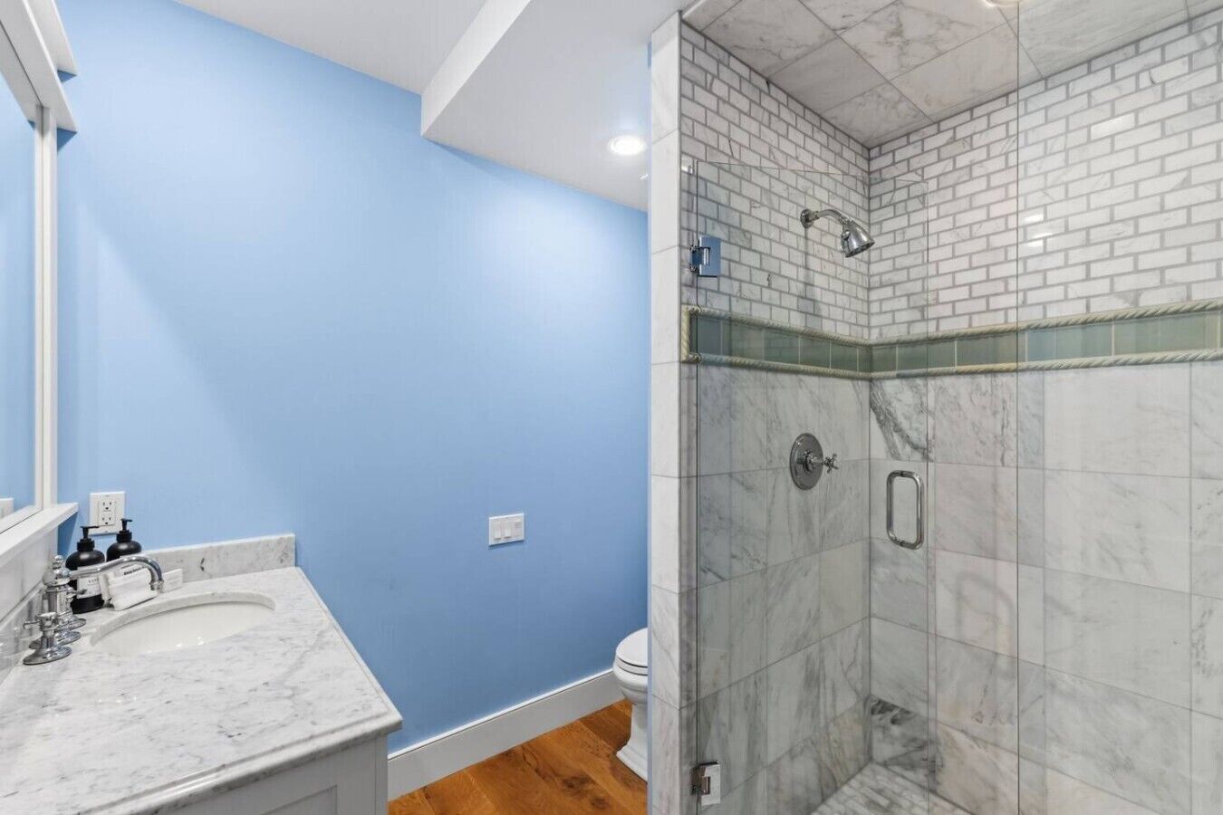 Een badkamer met een blauwe wand, een marmeren wastafel en een douchecabine met glazen wanden.