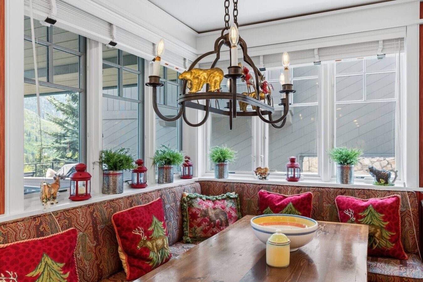Un coin salon accueillant avec un banc et une table, un lustre décoratif et des plantes en pot disposées sur un rebord de fenêtre.