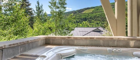 A hot tub with a stone edge and a view of a house and forest.