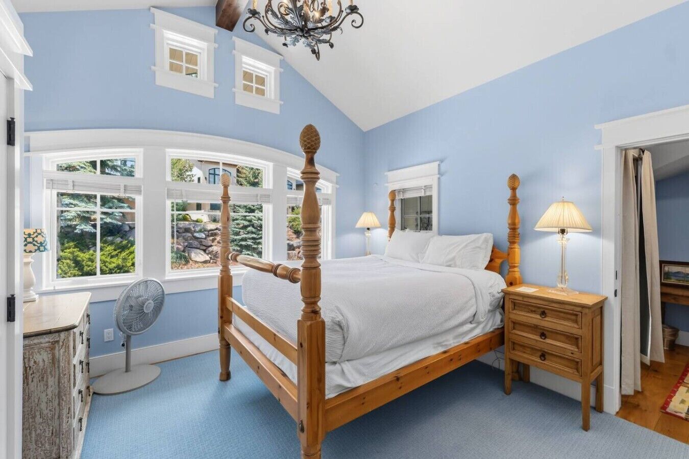Ein Schlafzimmer mit Himmelbett, Nachttisch mit Lampe, Ventilator und Blick ins Freie durch große Fenster.