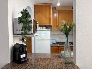 A kitchen with wooden cabinets, a white refrigerator, a microwave, a toaster, and a plant on the counter. - Comfort and sunshine: apartment near beach, center and community pool (Torrevieja)