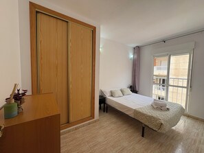 A bedroom with a bed, a wooden wardrobe, a small bedside table, and a window with a view of buildings. - Comfort and sunshine: apartment near beach, center and community pool (Torrevieja)