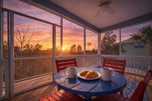 A covered outdoor seating area with a table and chairs, overlooking a scenic sunset view. - 7018 Rookery 3 New Listing 2 Pools 1 min to Beach (Gulf Shores)
