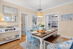 A dining area with a wooden table, blue chairs, a hanging light fixture, and a wall-mounted mirror. - 7018 Rookery 3 New Listing 2 Pools 1 min to Beach (Gulf Shores)