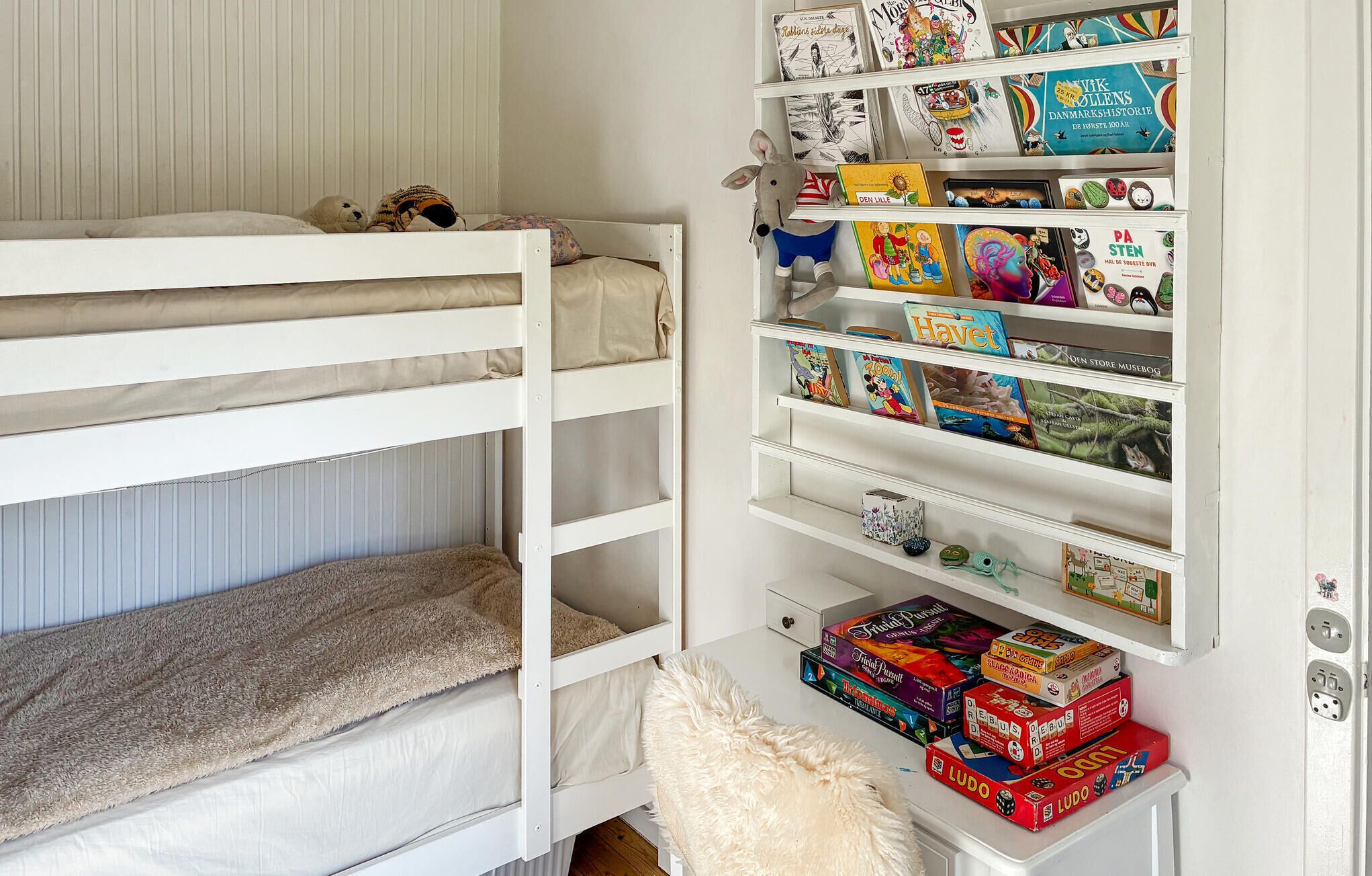 Ein Stockbett mit einer Schubladenkommode daneben, auf der Bücher und Gesellschaftsspiele liegen.