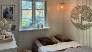 Ein Schlafzimmer mit Bett, Fenster mit Blick, einer Wanddekoration mit Baum und einem Nachttisch mit Kerzen und Blumen.