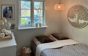Ein Schlafzimmer mit Bett, Fenster mit Blick, einer Wanddekoration mit Baum und einem Nachttisch mit Kerzen und Blumen.