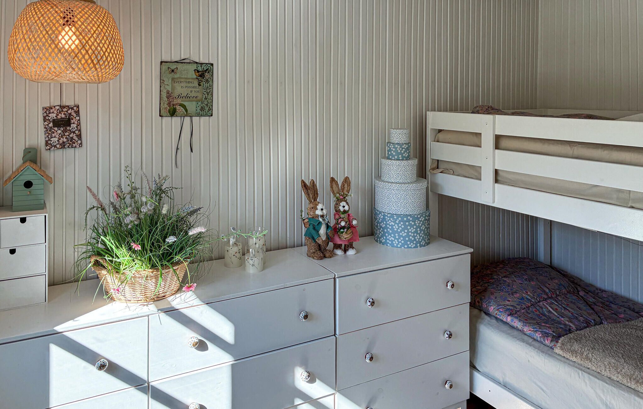 A child's room with a bunk bed, dresser, decorative items, and a hanging light fixture.