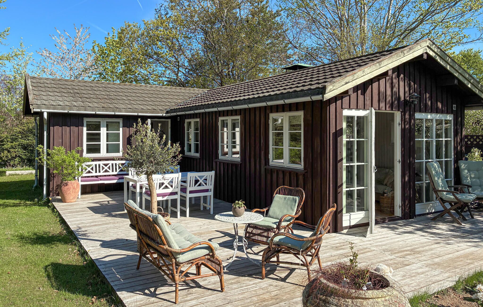 Una cabaña de madera con terraza, muebles de mimbre y una pequeña mesa.