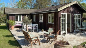 Eine Holzhütte mit einer Terrasse, Korbmöbeln und einem kleinen Tisch.