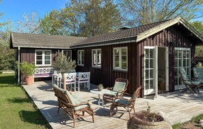 Eine Holzhütte mit einer Terrasse, Korbmöbeln und einem kleinen Tisch.