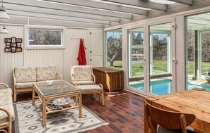A sunroom with wicker furniture, a glass table, and a view of a swimming pool.