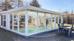 Una piscina con copertura in vetro, un patio e mobili da esterno.