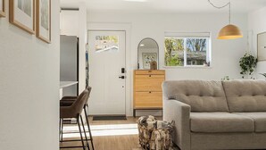A living room with a sofa, a coffee table, a dining area with chairs, and a kitchen area with a refrigerator. - Happy's Hideout, Downtown w/ Private Lawn (Ellensburg)