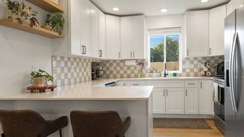 A kitchen with white cabinets, a large island with two chairs, a window with a view, and a refrigerator.