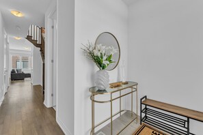 A hallway with a staircase, a console table with a vase of flowers, and a round mirror.