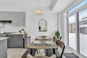 A modern kitchen with grey cabinets, a dining table set for four, and a large window offering a view of a snowy landscape.