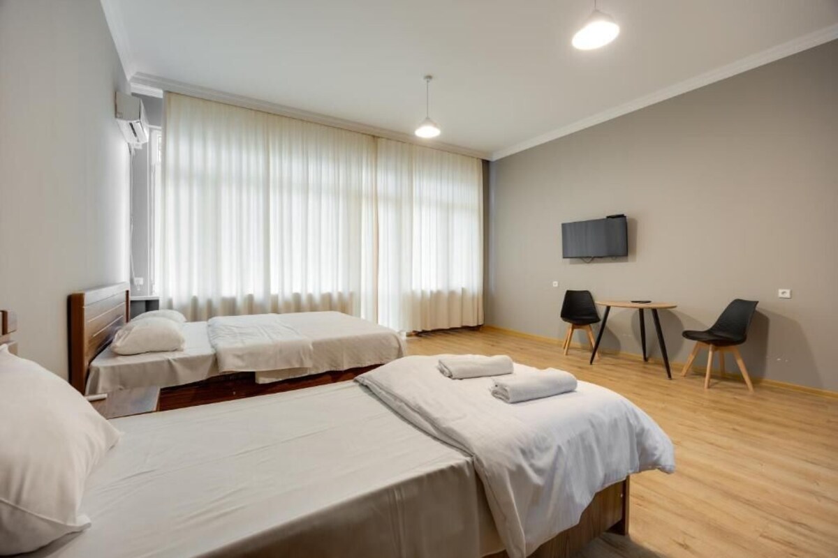 A hotel room with two beds, a TV, a small table, and chairs.