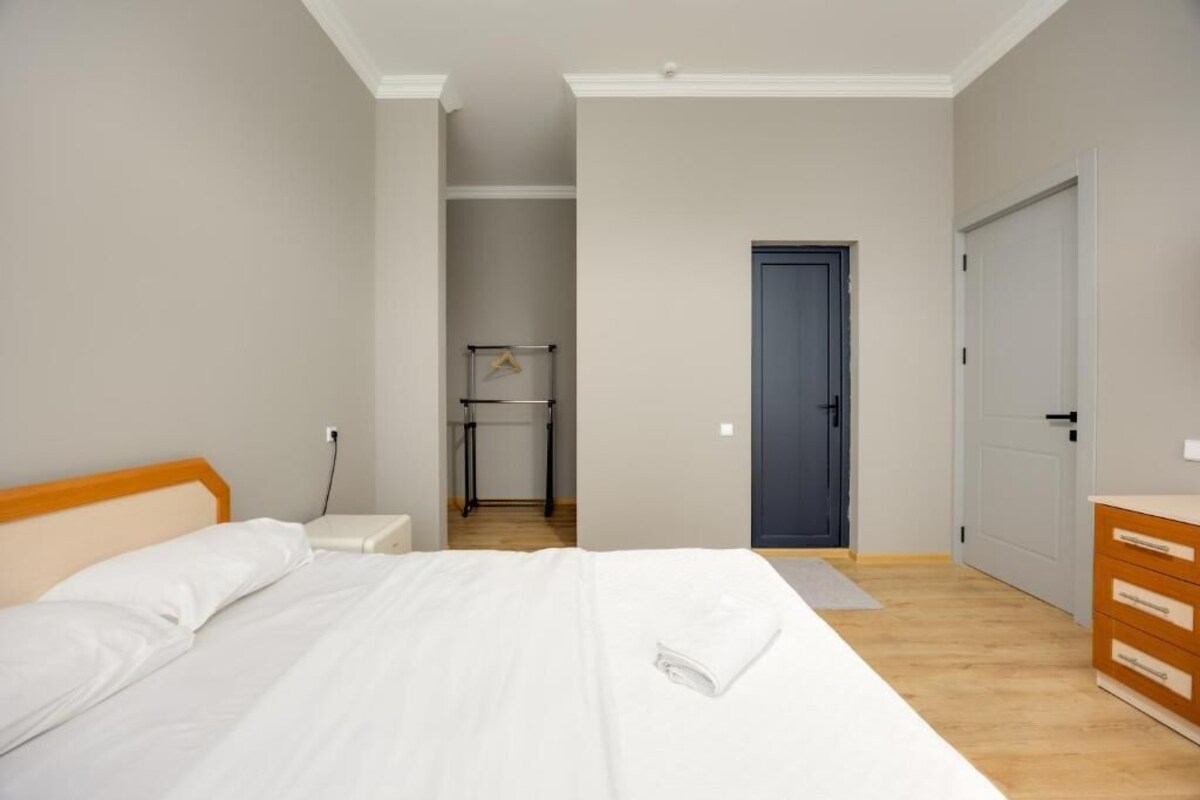 A bedroom with a bed, bedside table, a wardrobe, a door, and a small table with a hanger.