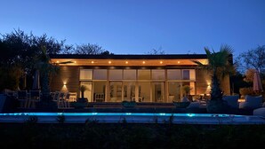 Ett modernt hus med pool, stora fönster och en uteplats.
