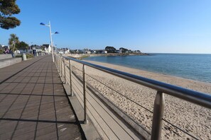 A seaside promenade with a wooden walkway, metal railing, and a clear view of the beach and ocean. - Bénodet – Everything within walking distance in a cosy duplex (BENODET)
