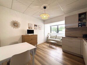 Eine moderne Küche mit Holzschränken, einem Esstisch mit Stühlen, einer Couch und einem großen Fenster mit Blick auf Grünflächen.